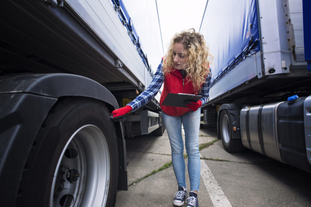 An image of a female inspector looking at two semi trucks.