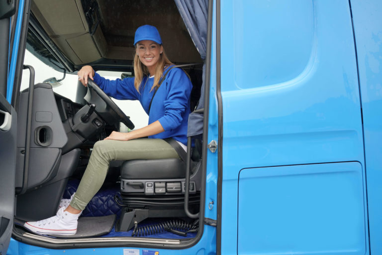 A female truck driver sitting in the cab of a truck.