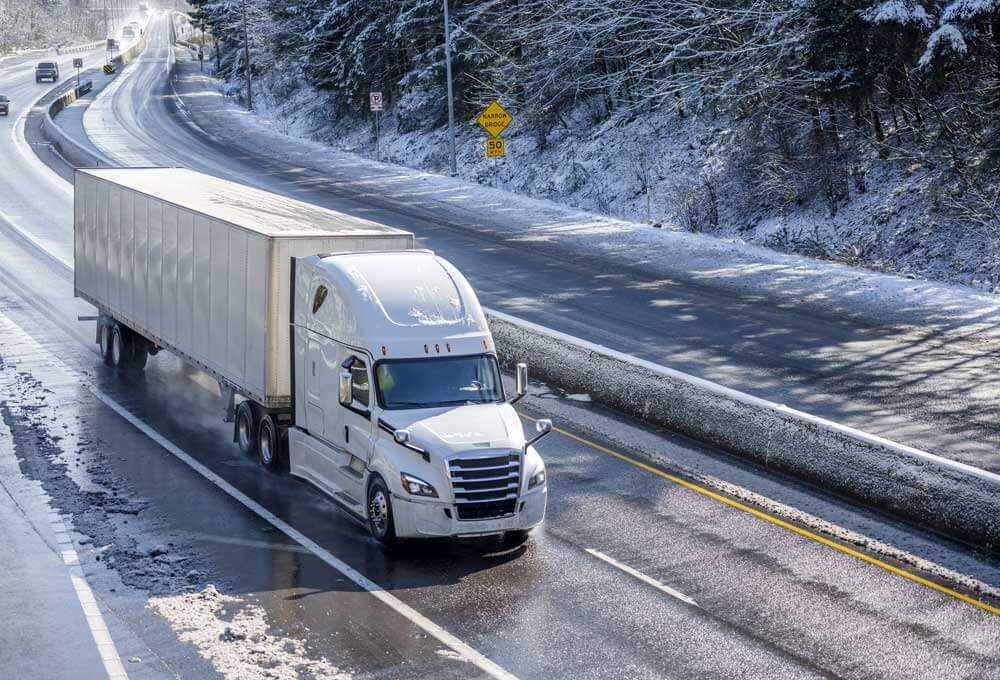 An image of semi truck driving on a snowy strip of highway.