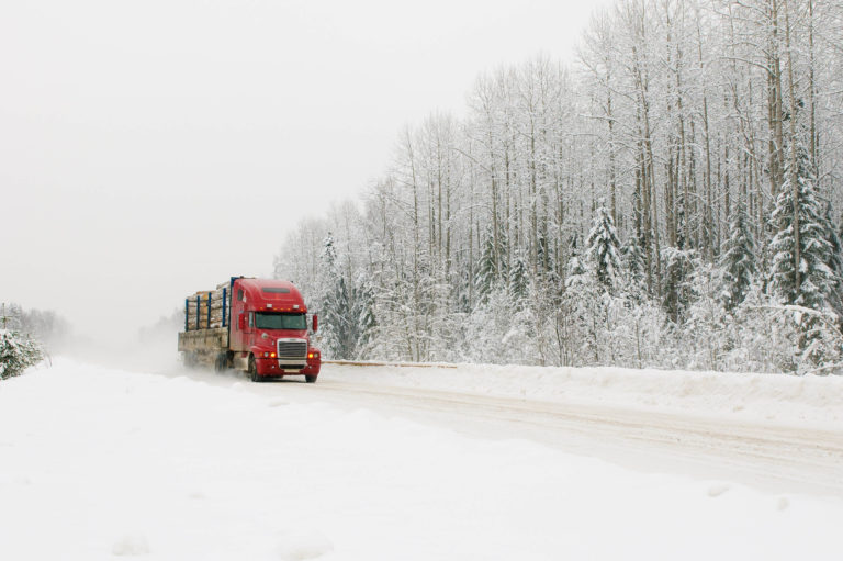 An image of a truck driving down the road on an incredibly snowy day.